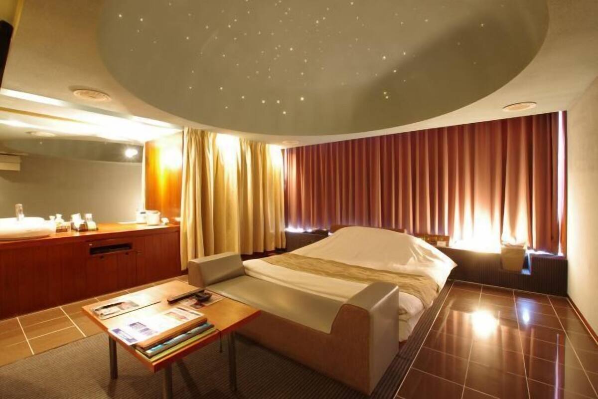 A hotel room with a bed, a desk, a chair, a mirror, and curtains.