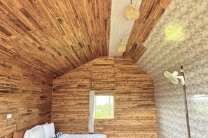 Une pièce de cabane en bois avec un plafond en pente, un lit, une fenêtre et une lampe.