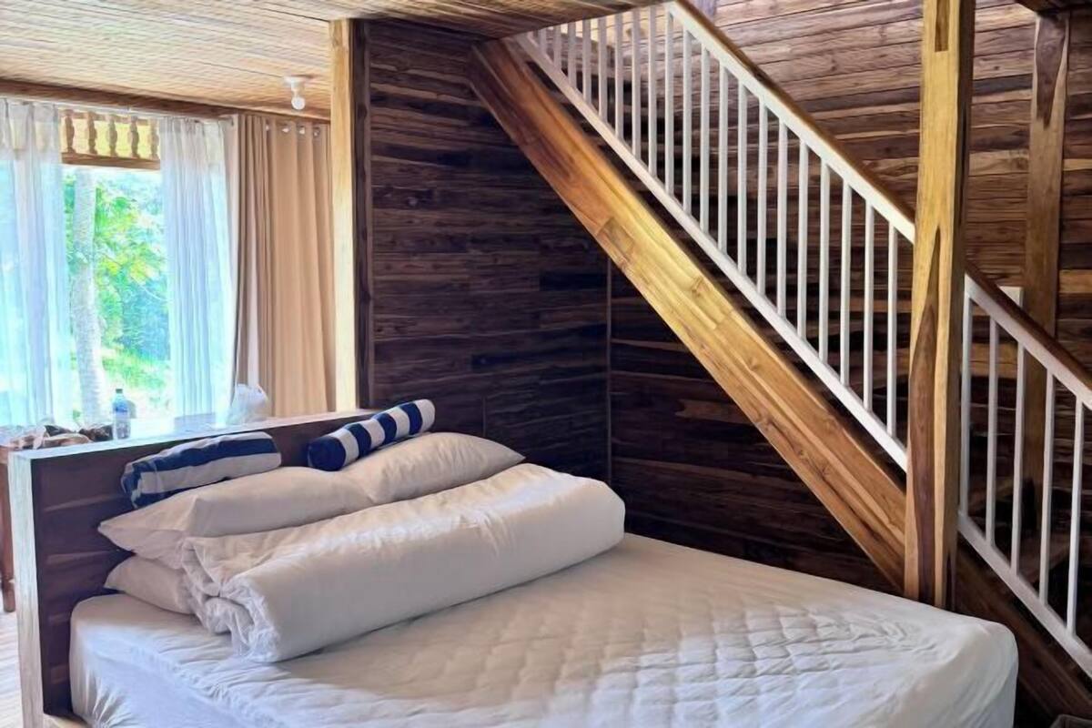 A bedroom with a wooden staircase, a bed with white bedding, and a window with curtains.