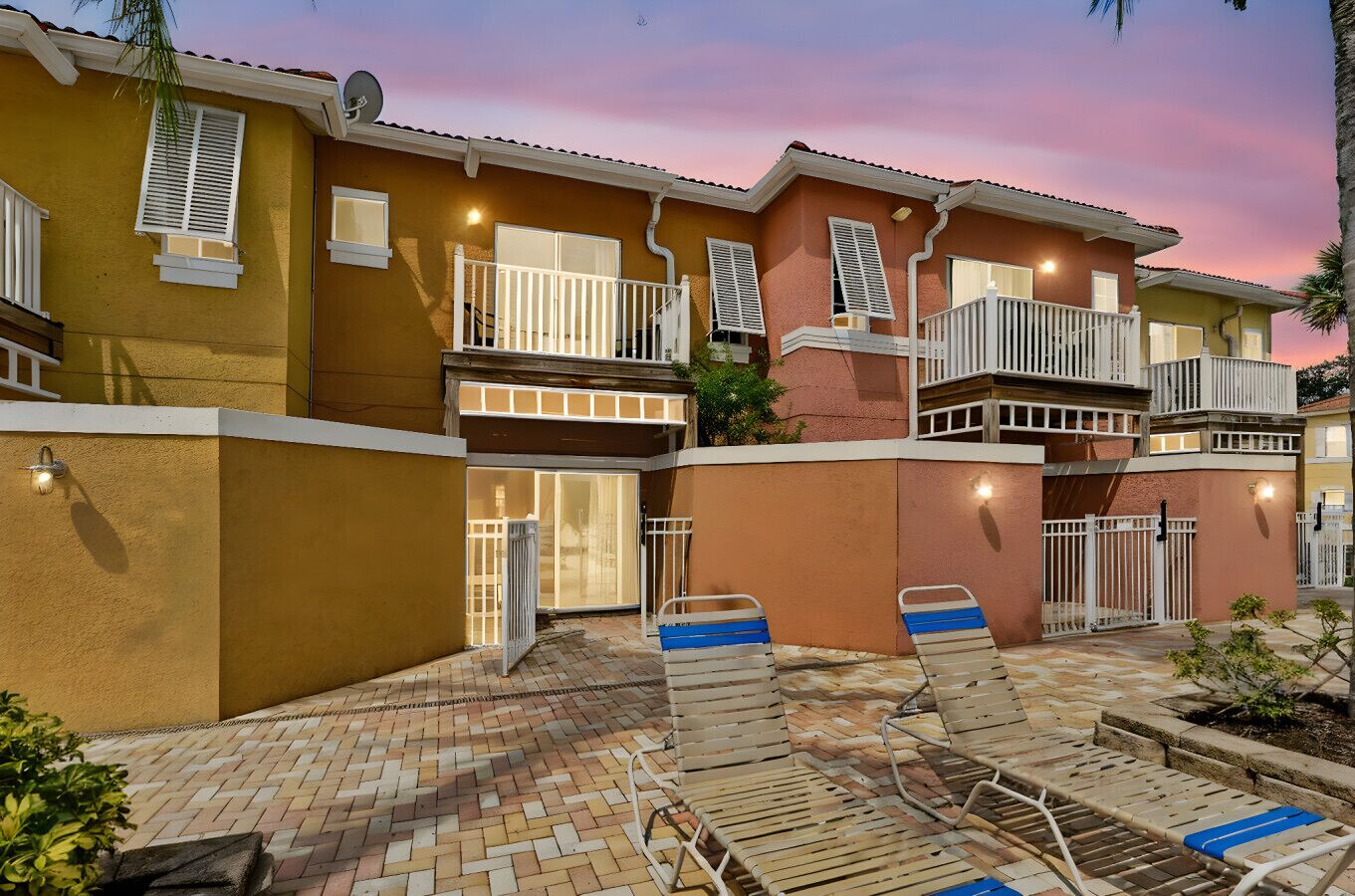 A multi-story residential building with balconies, a brick patio, and lounge chairs.