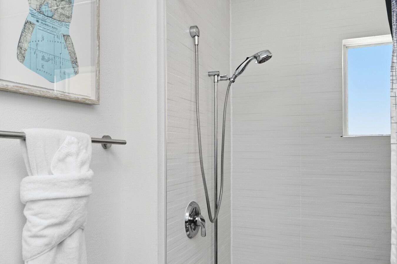 Ein Badezimmer mit Dusche, einem Handtuchhalter mit weißem Handtuch und einer gerahmten Karte an der Wand.