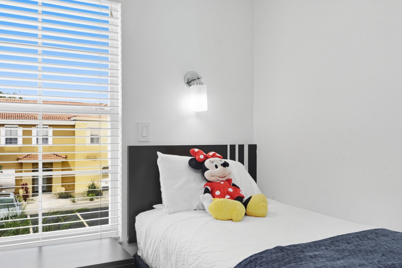 Una camera da letto con un letto, un peluche di Topolino e una finestra con persiane.