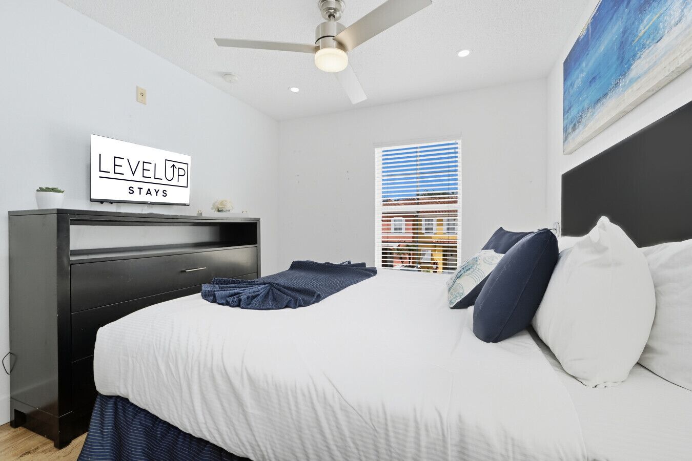 A bedroom with a bed, a dresser, a ceiling fan, a window with blinds, and a sign on the wall.