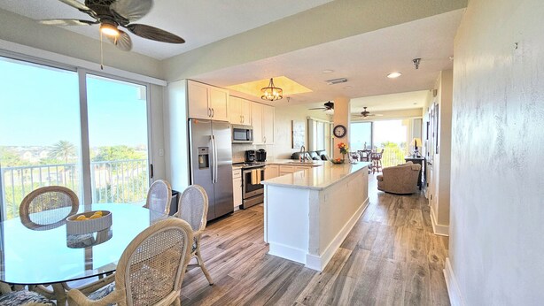 A modern kitchen with a central island, large windows, and a dining area with wicker chairs. - 🌴 "Blue Horizon at Surf Club" 🌅 Ocean Views 3rd Floor Corner Wraparound Balcony! (Palm Coast)