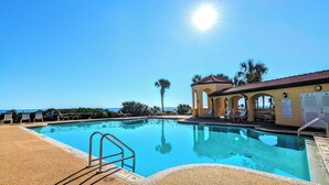 A clear blue pool with a lifeguard stand, lounge chairs, and a building with arches and a clock. - 🌴 "Blue Horizon at Surf Club" 🌅 Ocean Views 3rd Floor Corner Wraparound Balcony! (Palm Coast)