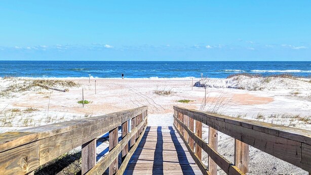 A wooden boardwalk leading to a beach with a clear view of the ocean.