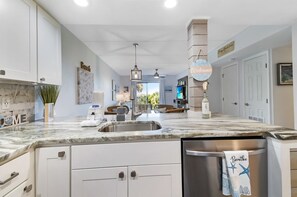 A modern kitchen with a marble countertop, stainless steel appliances, and a view to the living area.