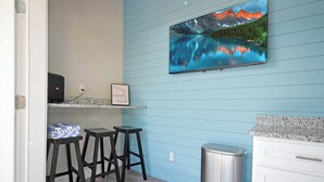 A kitchen with a blue wall, a TV mounted above a counter, two stools, a trash can, and a cabinet.