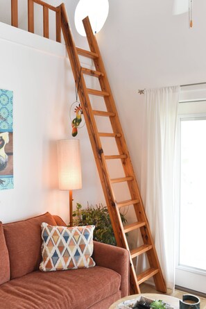 Une échelle en bois appuyée contre un mur, une lampe, un coussin et une fenêtre avec des rideaux.