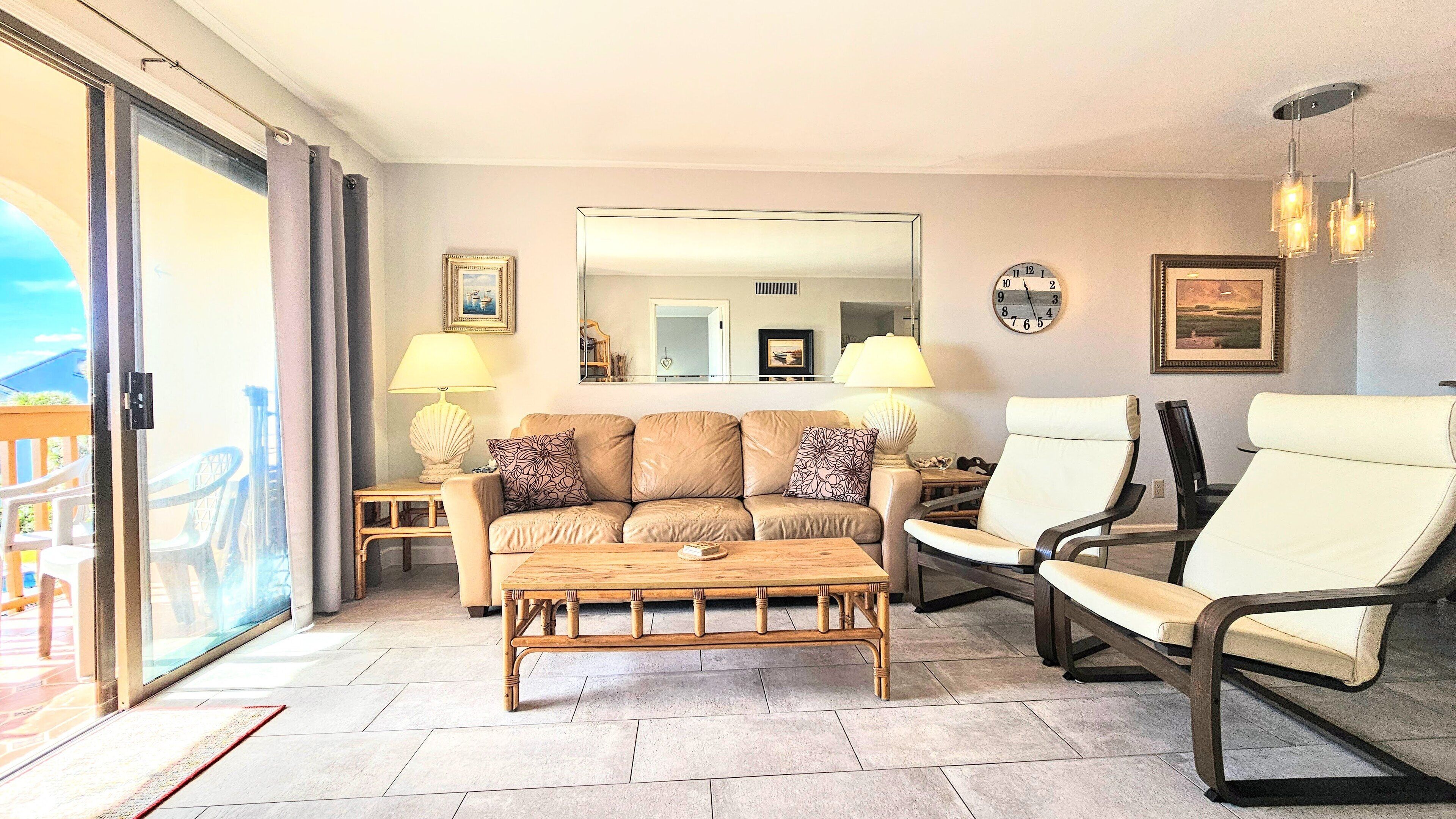 A living room with a sofa, two armchairs, a coffee table, and a dining table. There are two lamps, a clock, and a mirror on the wall.