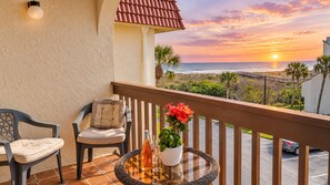 A balcony with a view of the sunset over the ocean, a wicker table with a bottle and glasses, and two chairs. - "Casatawaves" Ocean View Villa🌴Awesome Resort Pools! Trolley! (Saint Augustine)