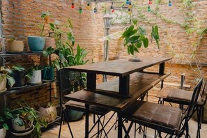 A rustic brick wall with a wooden table and chairs, surrounded by potted plants. - New York Loft & Japanese Magic by V4Skin (Bangkok)