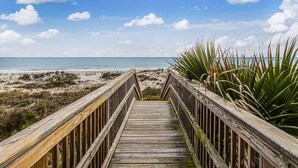A wooden boardwalk leading to a beach with a clear sky and clouds.