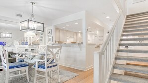 A modern kitchen with white cabinetry, a dining area with a round table and chairs, and a staircase with grey carpeted steps.