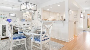 A modern kitchen with white cabinetry, a glass dining table, and blue-striped chairs.