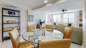 Un coin repas avec une table en verre, des chaises rembourrées et une étagère en bambou agrémentée de paniers.