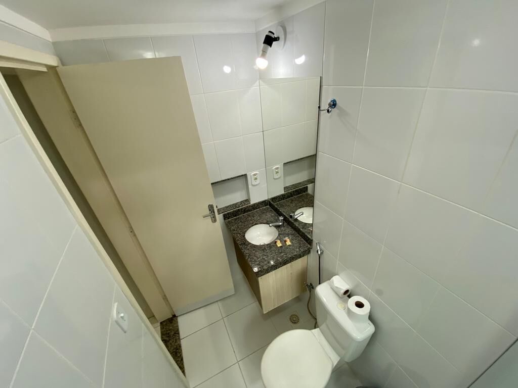 Et lille badeværelse med hvide fliser, toilet, vask og brusebad.