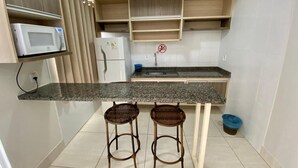 A compact kitchen with a granite countertop, two wicker stools, a microwave, and a refrigerator. - diRoma Lacqua Caldas Novas (Caldas Novas)