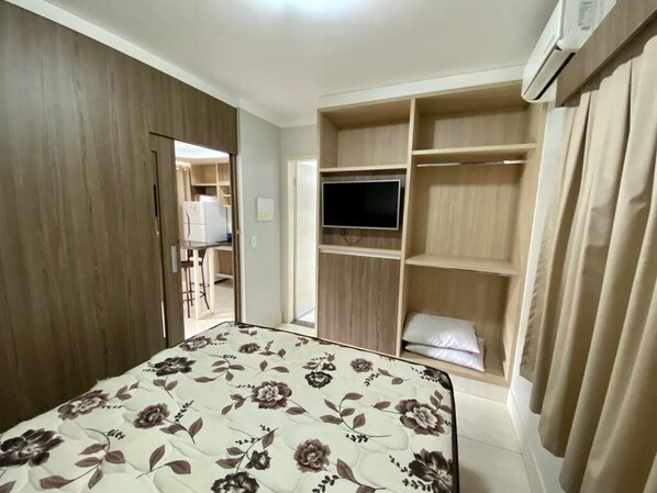 Un dormitorio con cama, televisor, armario y ropero.