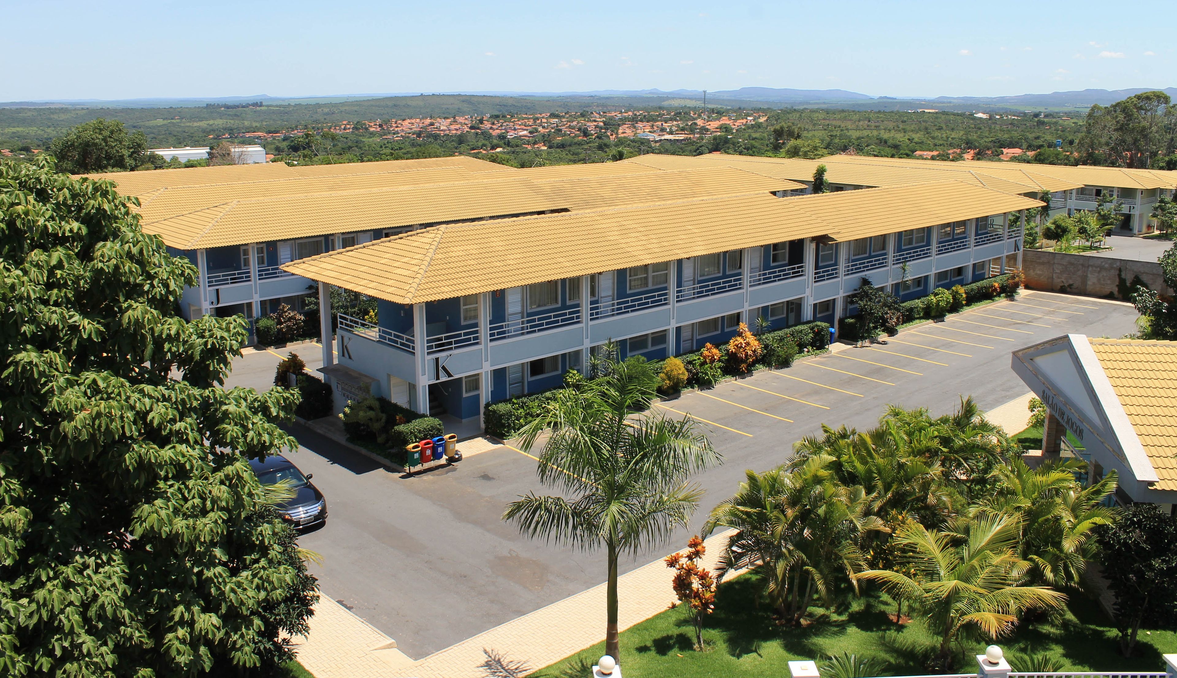 A hotel with multiple floors, a parking lot, and a view of a distant town.