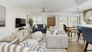 Un salon moderne avec un canapé, un pouf et un téléviseur à écran plat.