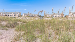 Un hôtel situé en bord de mer, composé de bâtiments à plusieurs étages, entouré de dunes de sable et de hautes herbes.