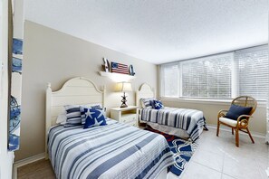 Een slaapkamer met twee bedden, een nachtkastje, een stoel en een raam met zonwering.