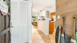A hallway with a wooden door, a kitchen area with a microwave, and surfboards leaning against a wall.