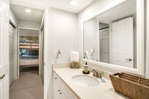 Une salle de bain d’hôtel avec un lavabo, un miroir et une vue sur la chambre.