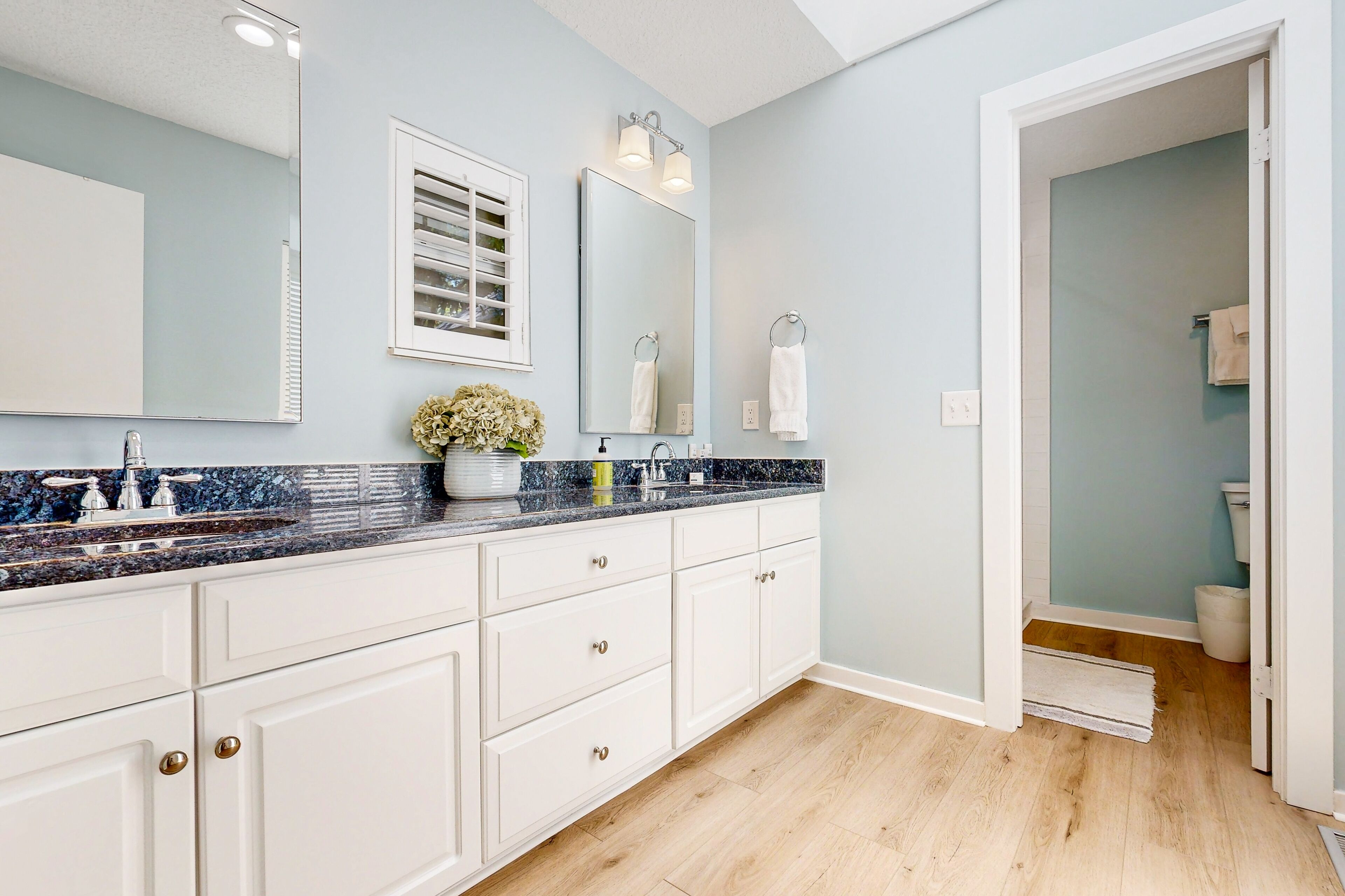 A modern bathroom with a large mirror, white cabinetry, and a marble countertop.