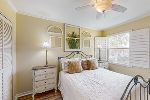 A bedroom with a bed, a nightstand, a lamp, a ceiling fan, and a window with shutters.