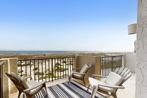 A balcony with two Adirondack chairs, a striped rug, and a view of the beach and ocean. - Oceanfront townhome with a furnished balcony, outdoor pool, & tennis (Fernandina Beach)