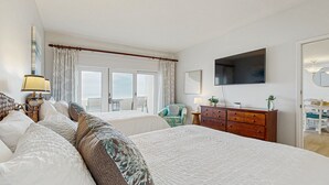 Quarto de hotel com duas camas, televisão, cómoda de madeira e vista para o exterior.