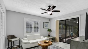 Un salon moderne avec un canapé blanc, une table basse en bois, un fauteuil en osier et un ventilateur de plafond.