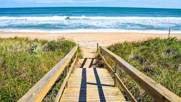 Une promenade en bois menant à une plage, avec des vagues en arrière-plan.