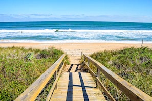 A wooden boardwalk leading to a beach with waves in the background.