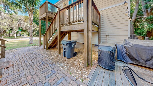 Une terrasse en bois avec une poubelle et un barbecue, un espace salon couvert et un escalier menant à une deuxième terrasse située à l’étage.