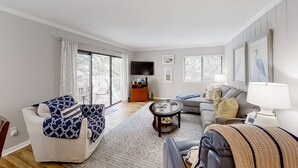 Een woonkamer met een bank, fauteuil, salontafel en een televisie. Er is een schuifdeur naar een balkon.