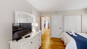 Een slaapkamer met een televisie op een dressoir, een bed met een blauwe deken, en witte deuren.