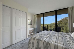 Une chambre avec un grand lit, une porte coulissante, une petite armoire et un balcon avec des chaises.