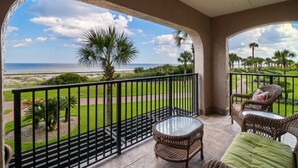 Ein Balkon mit Blick auf Strand und Meer, ausgestattet mit Korbmöbeln und einem Glastisch.
