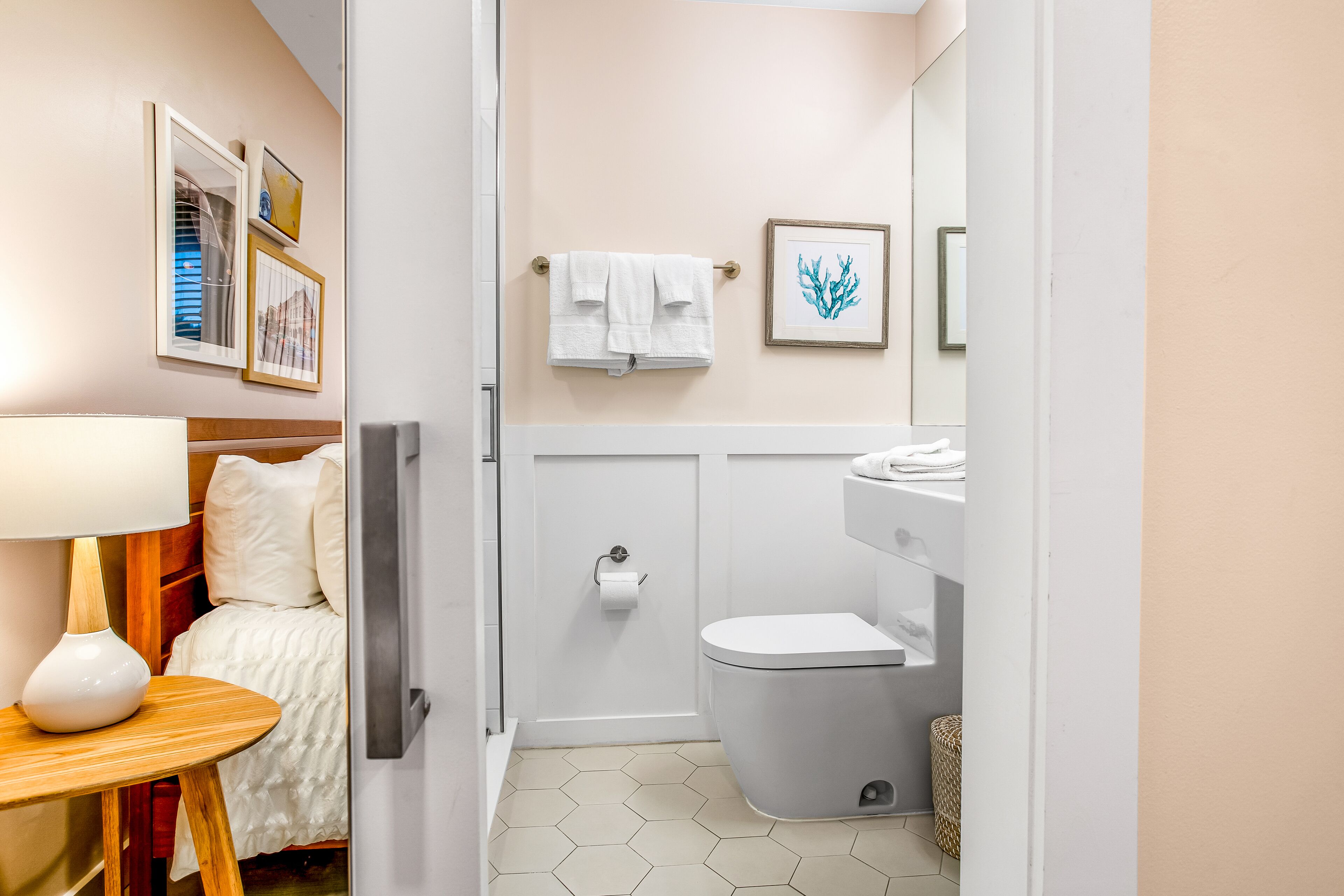 Ein Badezimmer mit Toilette, Waschbecken und Handtuchhalter. Ein Bett mit Holz-Kopfstütze und ein Tisch mit Lampe sind ebenfalls vorhanden.