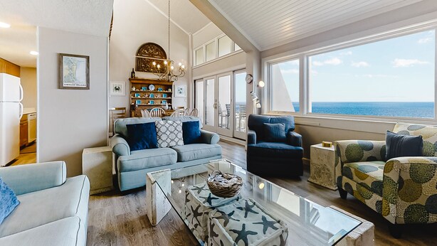 A spacious living room with a view of the ocean, featuring a sofa set, a coffee table, and a bookshelf. - Oceanfront condo with balcony, water views, AC & outdoor pool (Fernandina Beach)