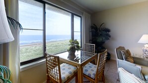 Una habitación con balcón, una mesa con sillas, un sofá y una planta en maceta.