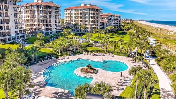 Un resort con varias edificaciones, una piscina central y vista a la playa.