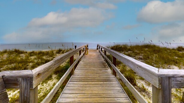 Une promenade en bois mène à la plage, avec des dunes herbeuses de chaque côté.