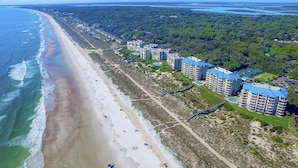 Luchtbeeld van een kustgebied met een strand, gebouwen aan het strand en een bebost gebied.