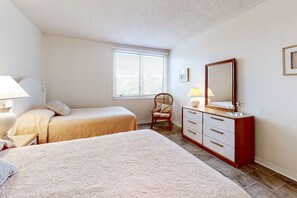 A bedroom with two beds, a dresser, a chair, and a window with blinds. - Oceanfront condo with large balcony, pool, central AC & views (Fernandina Beach)