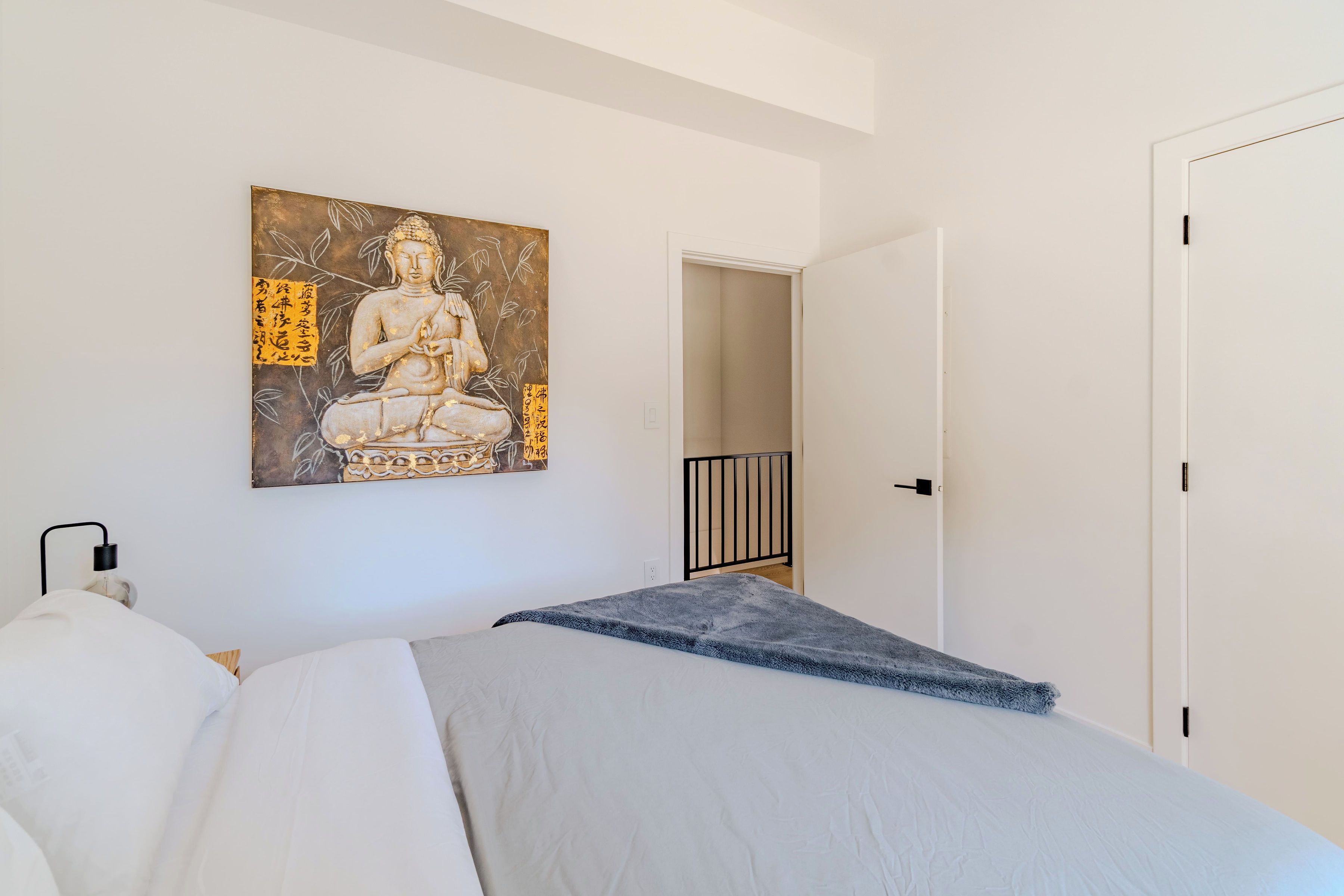 Une chambre à coucher avec un lit, un tableau accroché au mur, une porte et un interrupteur.