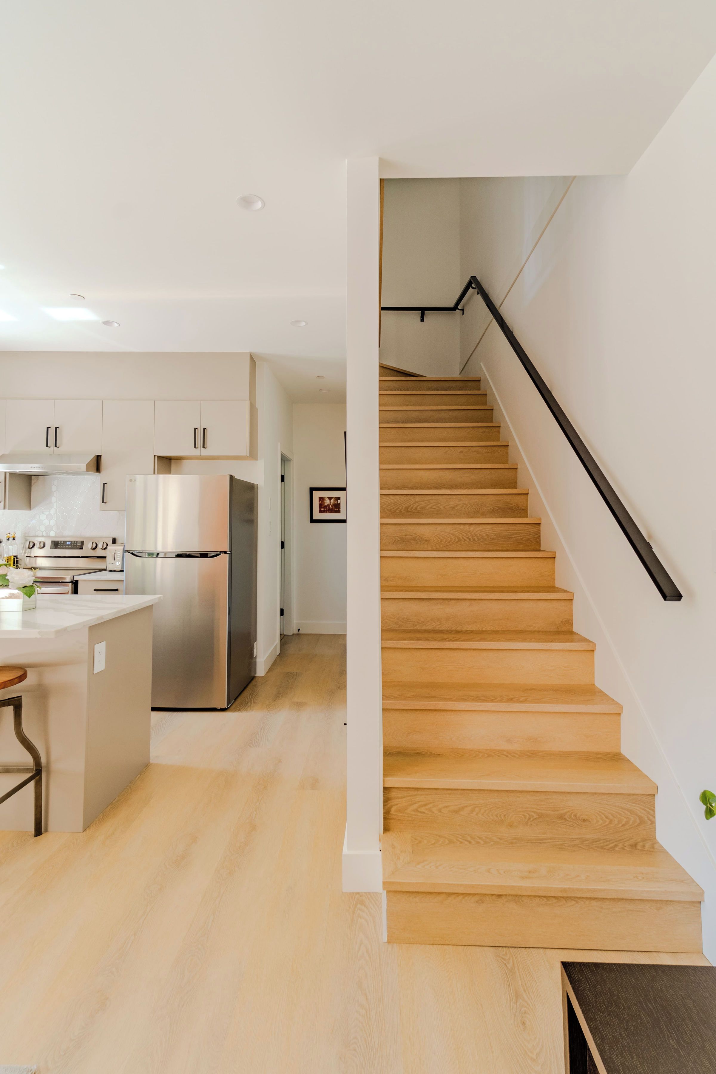 A modern kitchen with stainless steel appliances, a wooden staircase, and a minimalist design.